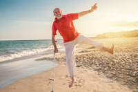 älterer Mann mit Gehstock springt am Strand fröhlich in die Luft